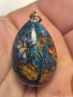 Front view of blue enamel egg pendant with floral motif and dot accents
