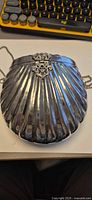 Angled view of shell-shaped silver-tone minaudière showing chain strap and overall form