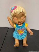 Front view of Baby Alive doll seated showing dress, hair bow and bracelet