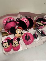 Entire Minnie Mouse cookware set laid out showing pots, kettle, lids, utensils, plush, and slippers