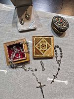 Group shot displaying earrings in box, two wooden boxes, filigree box, rosary, medal, figurine