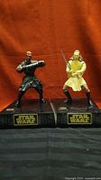 Front view of both Darth Maul and Qui-Gon Jinn coin banks on black bases