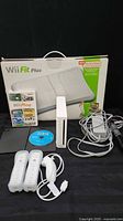 Full lot showing Wii console, two remotes, Nunchuk, cords, Wii Sports disc, Wii Play case, balance board box