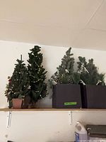Shelf with two potted artificial tabletop Christmas trees and two square planter arrangements