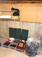 Overview of three clear totes filled with folded clothing, lids behind, pillow on shelf, bagged linens to side