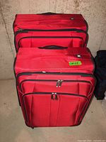 Two red Delsey suitcases front view showing wheels and zippers