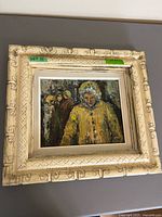 Framed oil painting showing figure in yellow parka, ornate cream carved frame