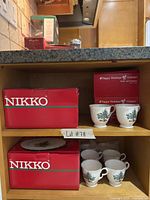 Boxed Nikko items on shelf showing two 12-piece sets, two 4-piece plate sets, loose cups