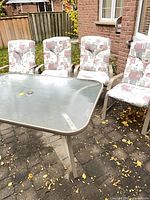 Full view of glass-top table with four matching cushioned chairs outdoors