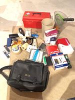 Overview of all items laid out: toolbox, satchel, twine, waste basket, bug-zapper, power strip, phone handset, remotes, supplies