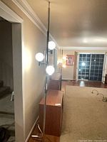 Full view of silver and black tension pole lamp with three globes in room