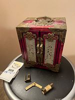 Front view of jewellery box with loose brass hardware pieces on table