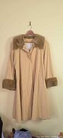 Full view of beige coat with faux fur collar and cuffs on hanger