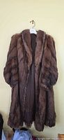Front view of full-length brown fur coat on hanger