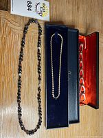 Three jewelry pieces: bead necklace, chain necklace in case, open-link bracelet in case