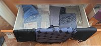 Drawer containing multiple folded scarves and stoles, some sealed in plastic, others draped over drawer front