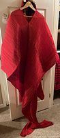 Front view of red Pleats Please kaftan hanging on hanger