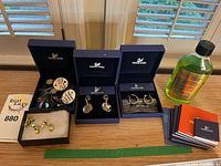 Overview of five earring pairs in Swarovski boxes, light green stud pair in foam box, manuals and cleaning solution bottle