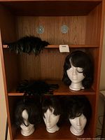 Shelf displaying four short dark wigs and feather shoulder pads