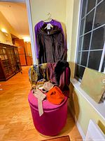 Group shot showing raincoat, sweater, scarves, hats on pink ottoman