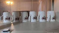 Six mugs upside down showing exterior floral pattern and gold handles