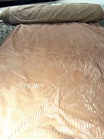 Bolt of pink striped upholstery fabric unrolled to show surface texture and quantity