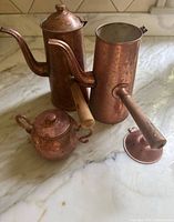 Two tall copper kettles and small lidded pot on countertop