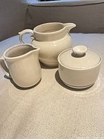 Three ceramic pieces: large pitcher, small creamer, lidded sugar bowl