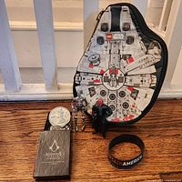 Full lot displaying Millennium Falcon case, Assassin’s Creed coin box with coins, two Star Wars figures, Captain America wristband