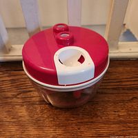 Red-lidded clear plastic food chopper on wood surface