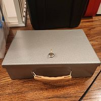 Closed grey metal lock box showing locked position and tan handle