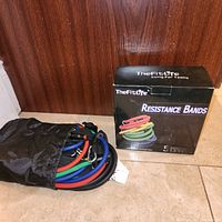 Retail box labelled TheFitLife Resistance Bands alongside fabric pouch containing coloured resistance tubes with clips