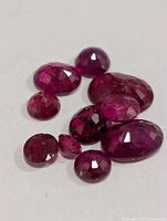 Group of nine loose faceted ruby gemstones displayed on white background