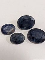 Four oval faceted dark blue sapphires on white surface