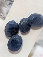 Four oval blue sapphires on white background, top view highlighting facets