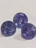 Three loose round violet-blue tanzanite stones on white background