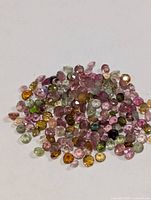 Pile of small round faceted multicolour tourmaline stones on white background