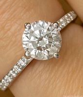 Close-up of round brilliant center diamond in four-prong setting on finger