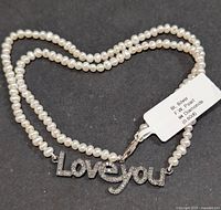Full view of pearl necklace forming heart shape with diamond “Love you” pendant and tag