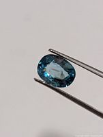 Close-up of blue zircon held in tweezers, showing color and cut