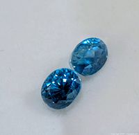 Close-up of both faceted blue zircons showing color and cut
