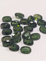 Group of oval faceted green chrome diopside gemstones on white background