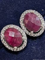 front view pair of earrings on blue background showing ruby centers and halo