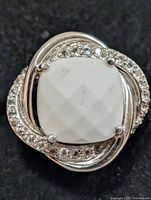 Top view showing white faceted cushion gemstone and swirl halo with clear stones