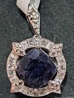 Front view of silver pendant showing sapphire center and white topaz halo