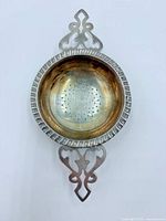 Top view showing fluted rim and ornate handle of silver tea strainer