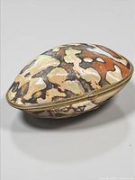 Side perspective of oval shell box showing brass trim and clasp