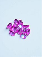Group of thirteen vivid pink oval sapphires on light background