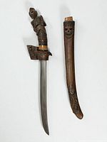Dagger unsheathed beside scabbard showing blade, hilt carving and scabbard skull motif