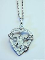 Close-up of pendant showing cherub, heart frame with stones, daisy accents, and bail with stone